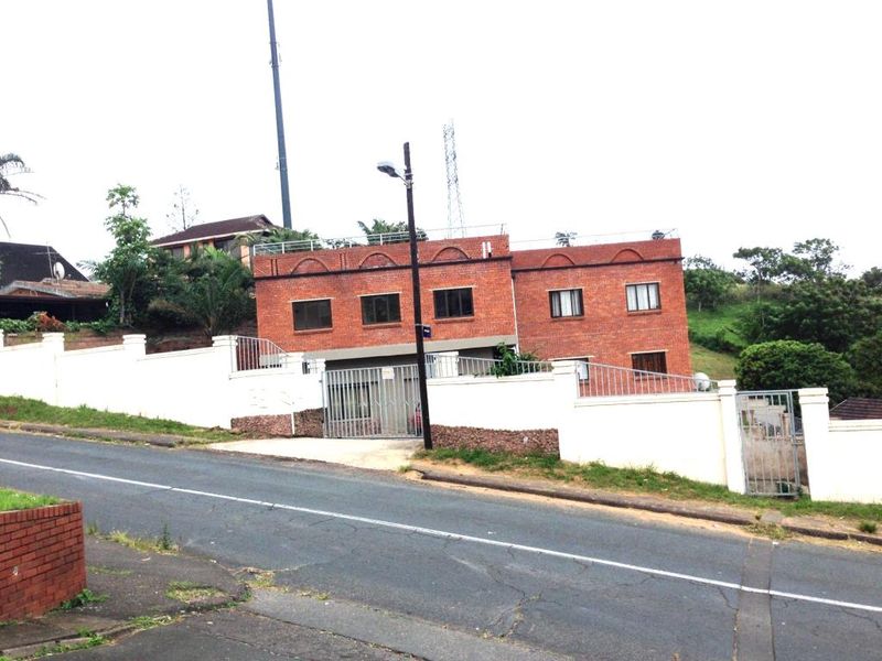 A street-level view of a two-story red brick apartment building featuring a secure perimeter wall, gated entrance, and metal security fencing.