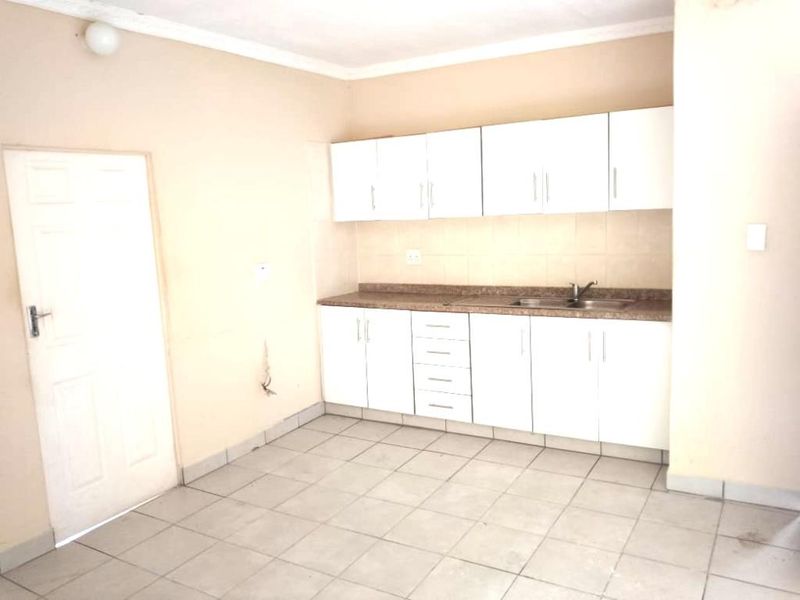 A functional kitchen area featuring white cabinetry, a laminate countertop, and tiled flooring, offering a blank canvas for potential updates.