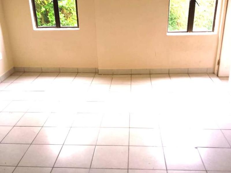 A bright, empty living area featuring neutral tiled flooring and two windows providing natural light.