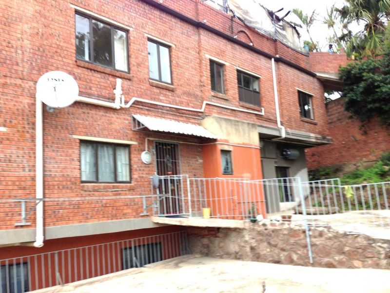 Exterior view of a multi-level brick apartment building featuring metal security gates, external plumbing, and a concrete patio area.