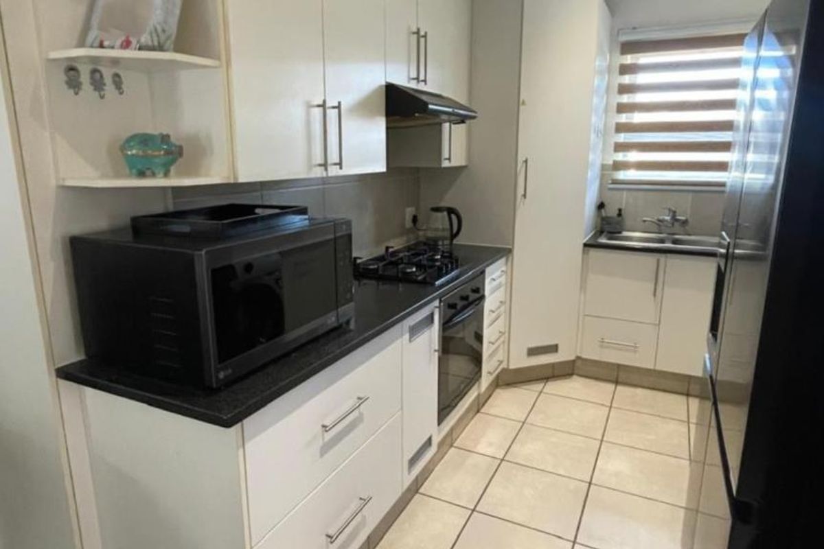 A functional kitchen featuring white cabinetry, dark countertops, a gas hob, built-in oven, and tiled flooring with a window for natural light.