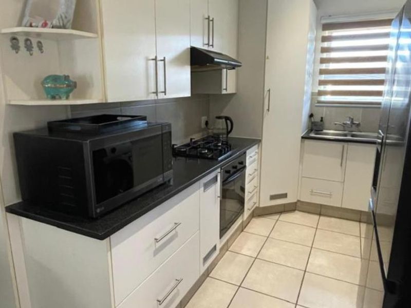 A functional kitchen featuring white cabinetry, dark countertops, a gas hob, built-in oven, and tiled flooring with a window for natural light.
