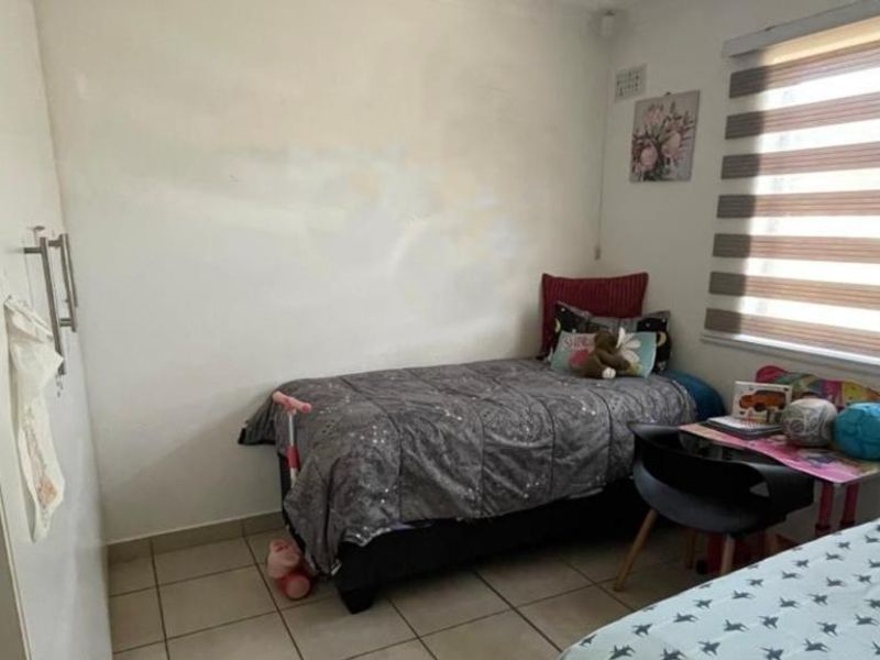 A compact bedroom featuring tiled flooring, a built-in wardrobe, and roller blinds. The walls show signs of wear and require cosmetic attention.