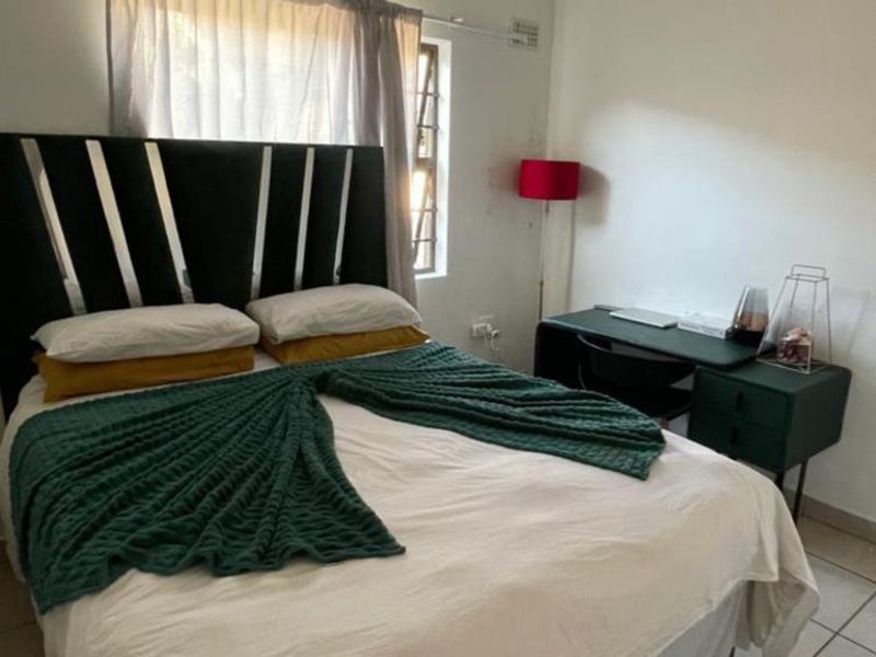 A functional bedroom featuring tiled flooring and a window with security burglar bars, providing a simple and practical living space.