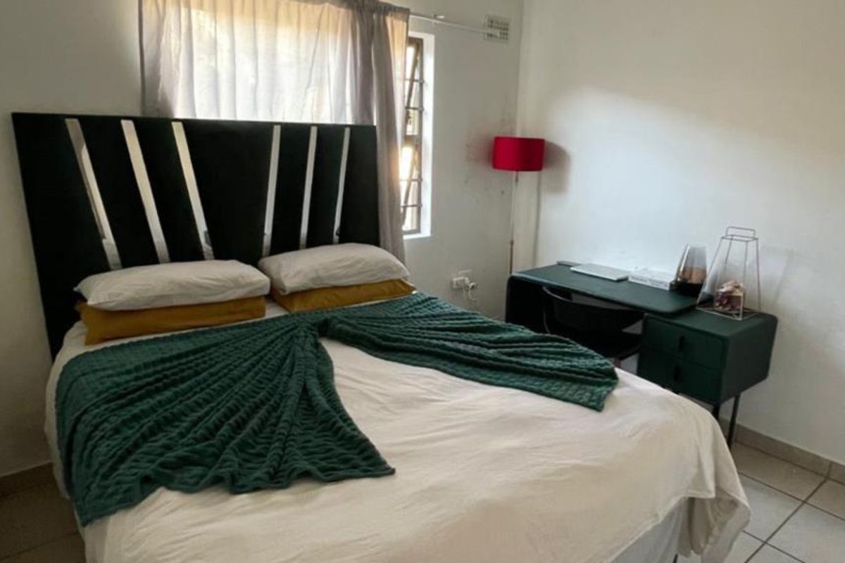 A functional bedroom featuring tiled flooring and a window with security burglar bars, providing a simple and practical living space.