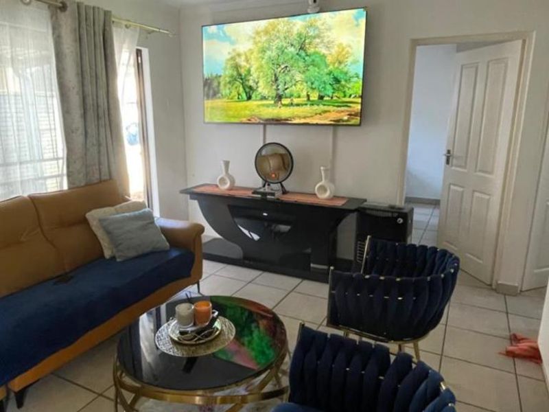 A living room featuring tiled flooring, natural light from a window, and access to adjacent rooms via internal doors.