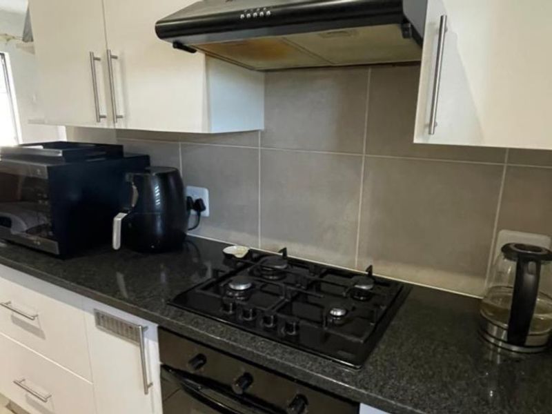 A functional kitchen area featuring a gas hob, built-in oven, extractor fan, granite countertops, and modern white cabinetry with a tiled backsplash.