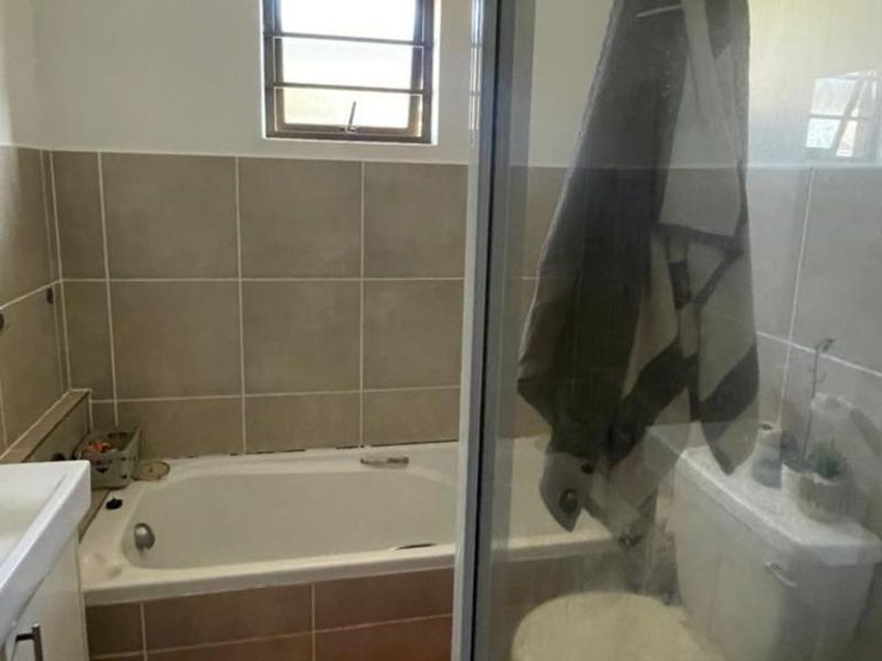 A functional bathroom featuring a bathtub, separate shower enclosure, vanity basin, and toilet with neutral wall tiling.