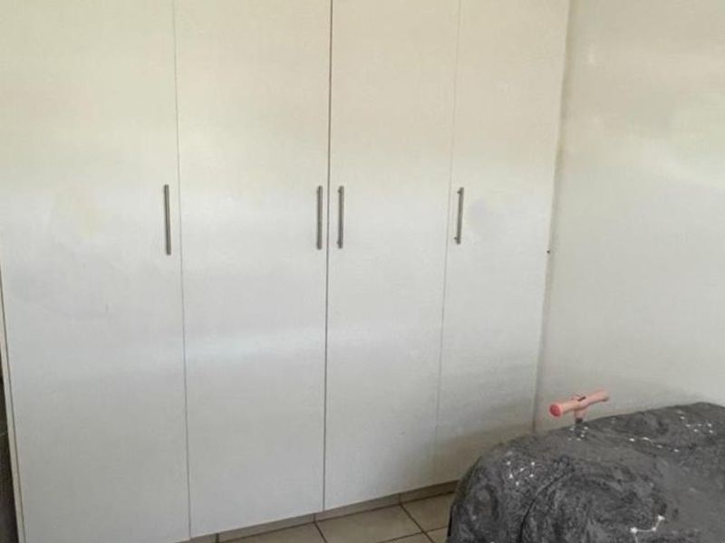 A bedroom featuring a large white built-in wardrobe with modern handles and tiled flooring.