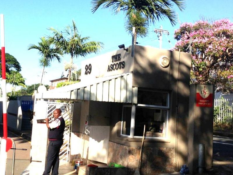 The entrance to The Ascots apartment complex featuring a security guard house and controlled boom gate access.