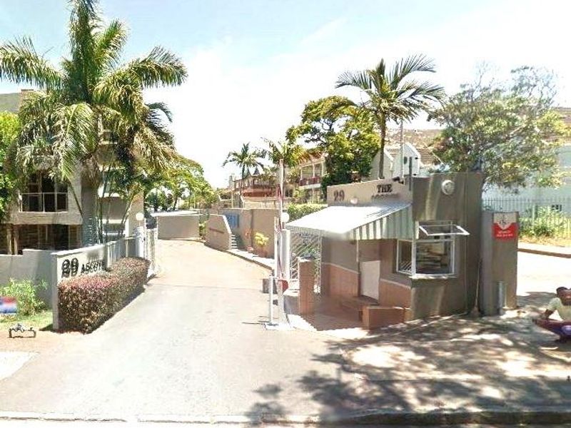 The entrance to the apartment complex features a security guard house, boom gate access, and established palm tree landscaping.