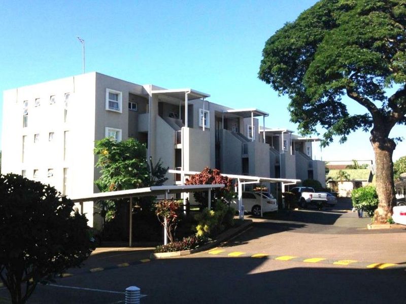 Exterior view of a multi-story apartment complex featuring covered parking carports, external stairwells, and private balconies.