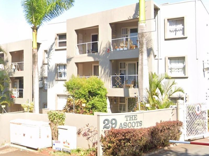 Front elevation of The Ascots apartment complex, featuring multi-level balconies with glass balustrades, secure gated entrance, and established landscaping.
