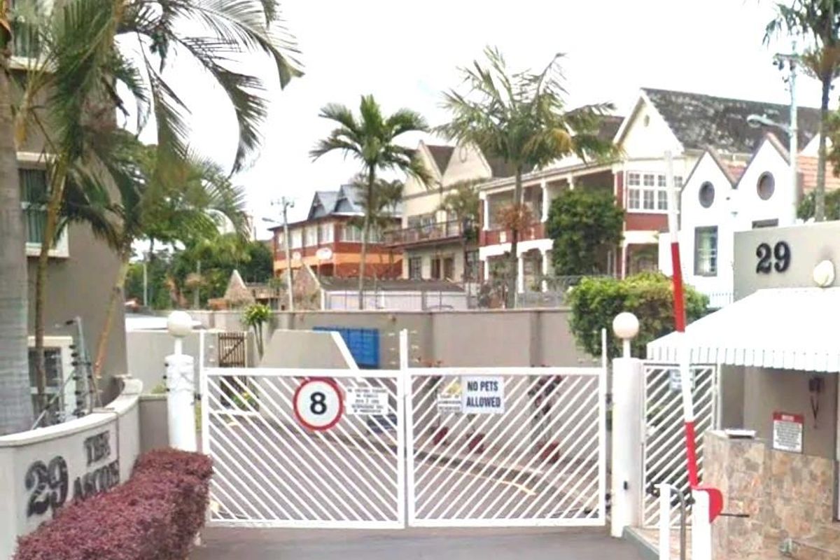 The entrance to the apartment complex features a secure gated access point with a boom gate and perimeter walling.