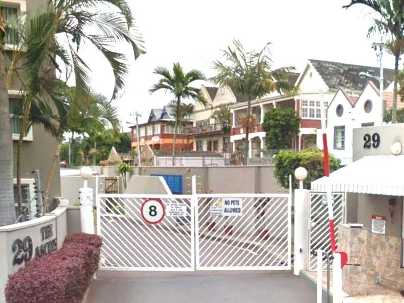 The entrance to the apartment complex features a secure gated access point with a boom gate and perimeter walling.