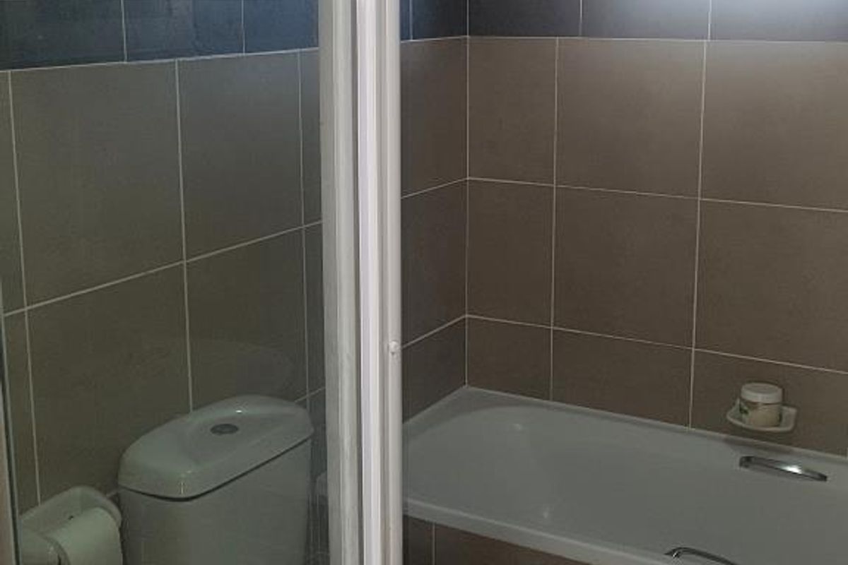 A functional bathroom featuring a built-in bathtub, a standard toilet, and neutral wall tiling with a decorative accent border.