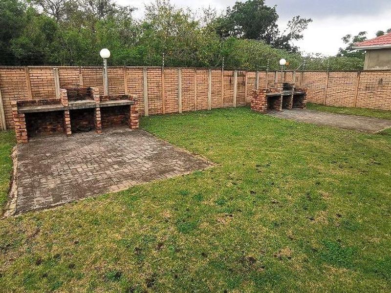 A spacious garden area featuring two built-in brick braai stations, paved patio sections, and a perimeter brick wall with electric fencing.