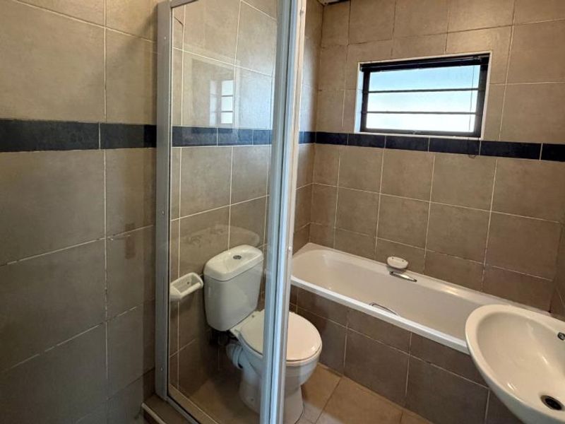 A functional bathroom featuring a shower enclosure, bathtub, toilet, and washbasin with neutral wall and floor tiling.