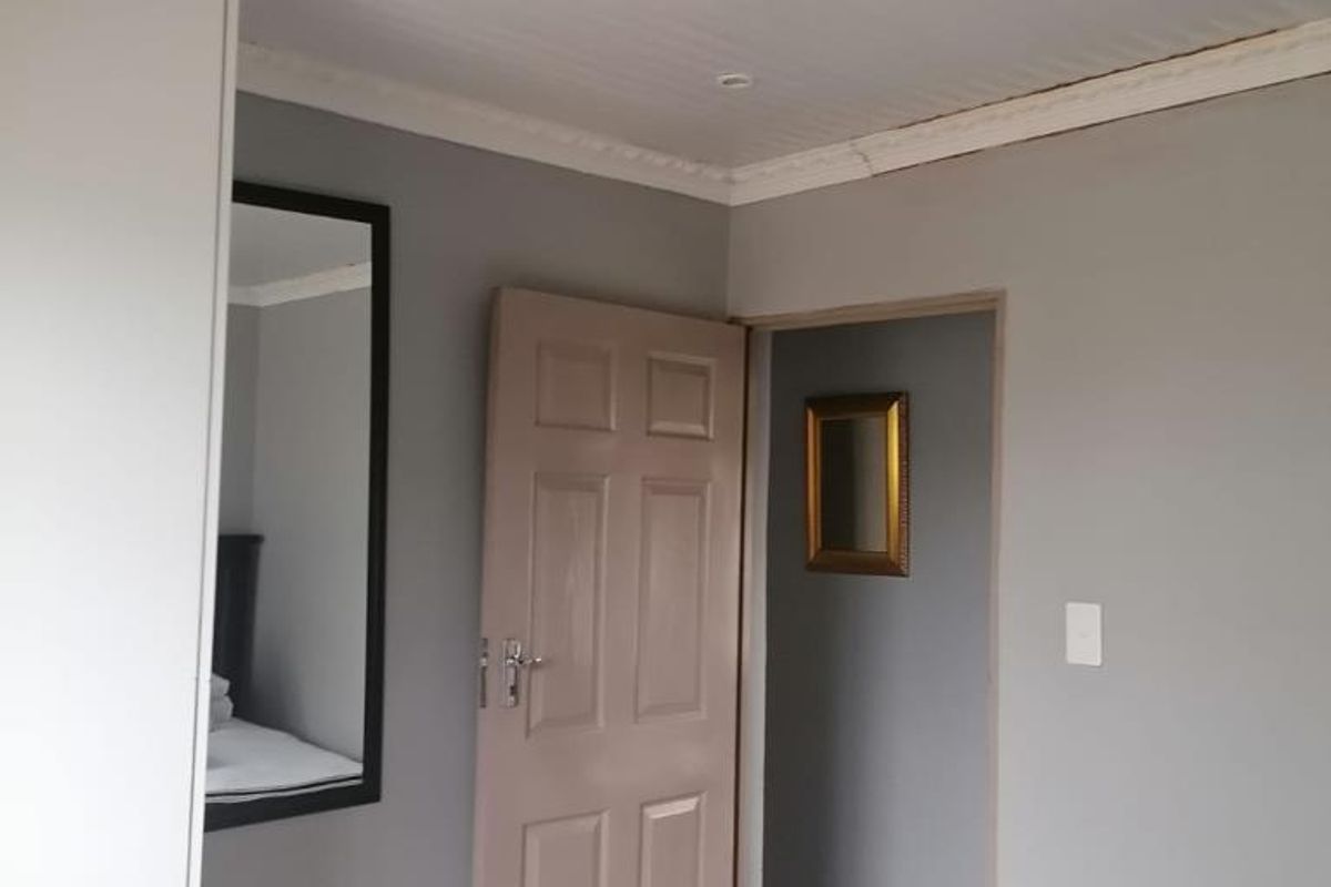 A bedroom featuring built-in cabinetry, a panelled door, and crown molding, leading into an adjacent hallway area.