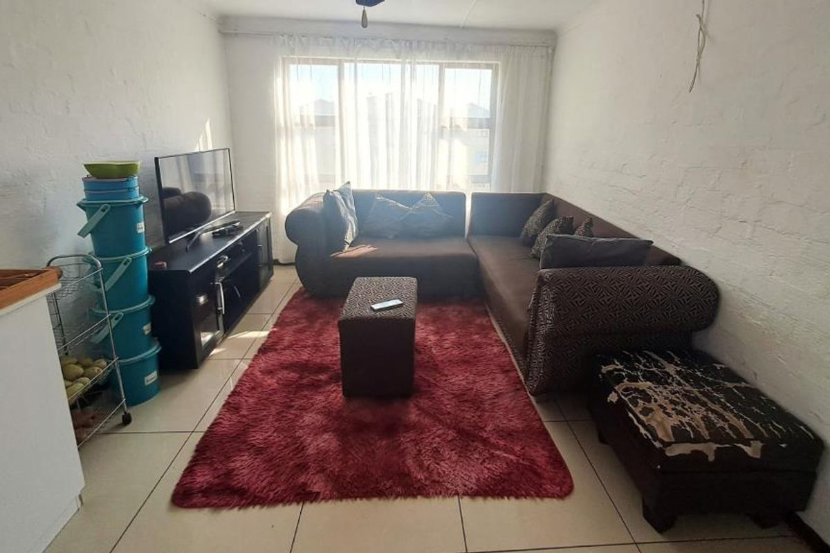 A living room featuring tiled flooring, textured walls, and a large window allowing natural light. The space includes visible ceiling wiring.