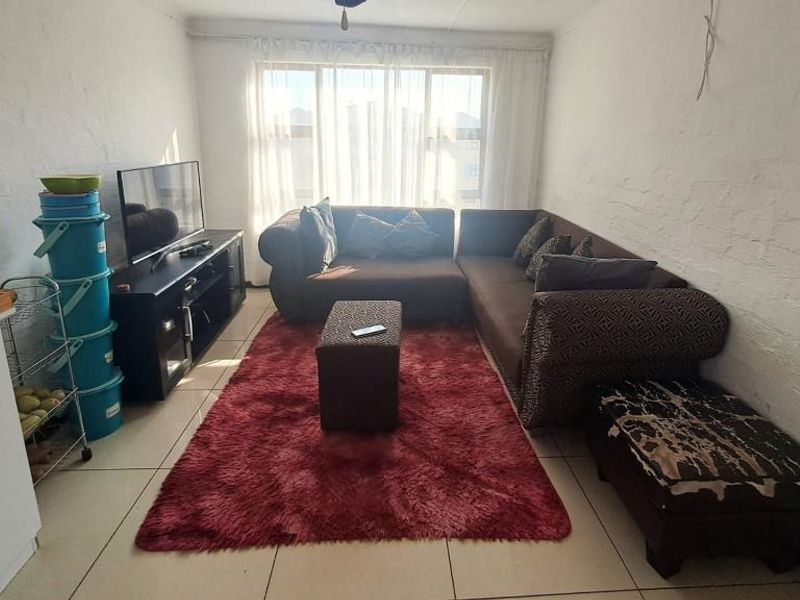 A living room featuring tiled flooring, textured walls, and a large window allowing natural light. The space includes visible ceiling wiring.