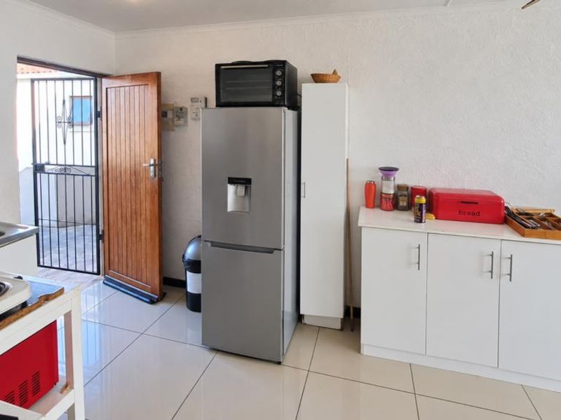 A functional kitchen area featuring tiled flooring, built-in cabinetry, a stainless steel sink, and direct access to an exterior security gate.