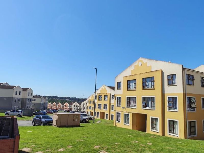 Exterior view of multi-story apartment complex featuring yellow and grey facades, paved parking areas, and surrounding green lawn spaces.