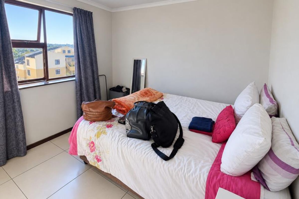 A bedroom featuring tiled flooring and an aluminium window frame, offering a functional space with natural light.