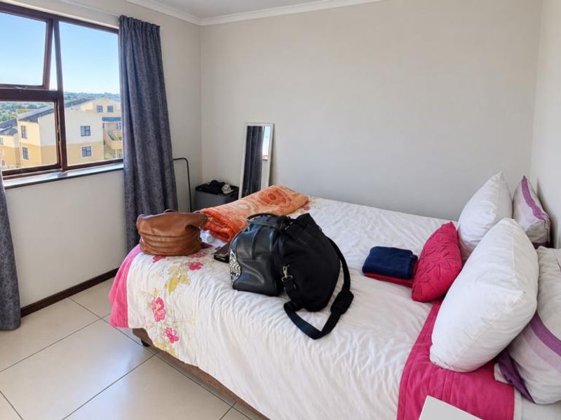 A bedroom featuring tiled flooring and an aluminium window frame, offering a functional space with natural light.