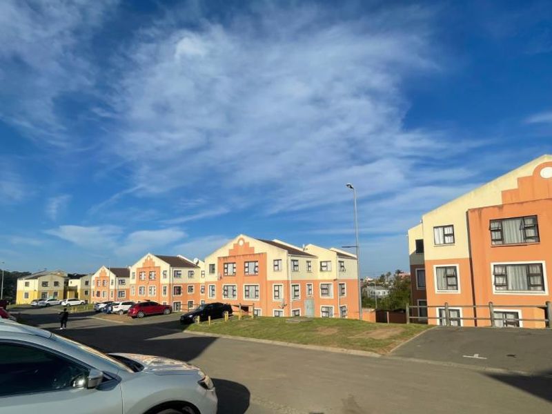 Exterior view of a multi-story apartment complex featuring paved parking areas and residential building facades under a clear blue sky.