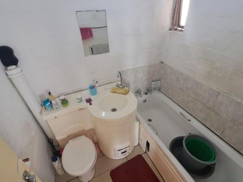 A compact bathroom featuring an integrated vanity and toilet unit alongside a standard bathtub with tiled splashback, requiring cosmetic updates.