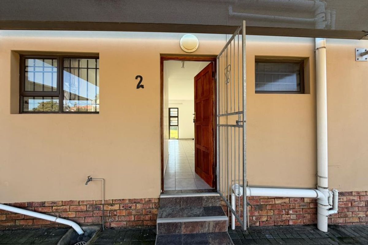 Front entrance of the apartment featuring a security gate, tiled steps, and exterior brick detailing.
