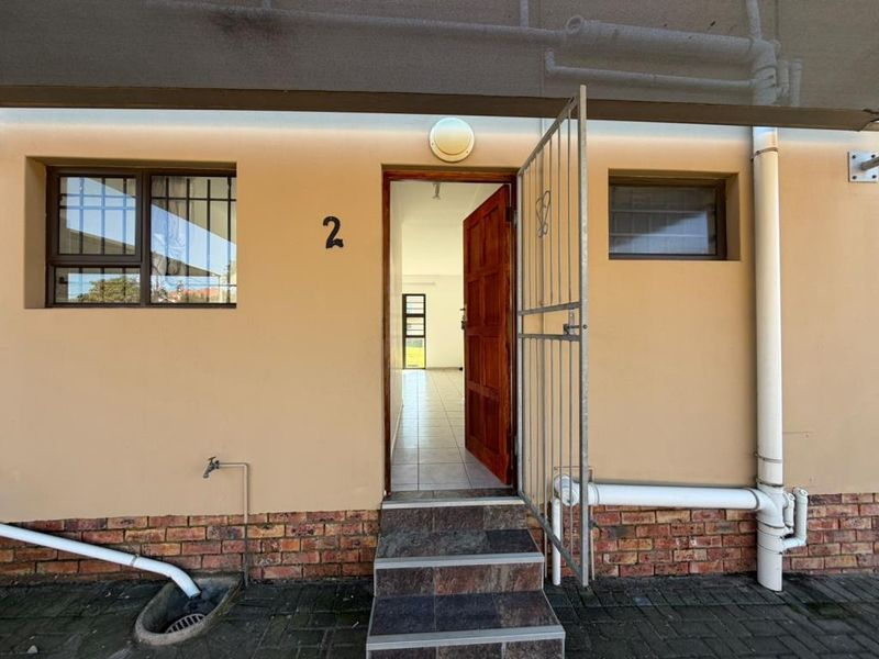 Front entrance of the apartment featuring a security gate, tiled steps, and exterior brick detailing.