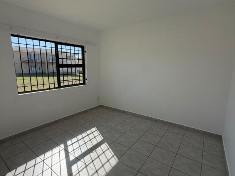 A bright, empty bedroom featuring neutral tiled flooring and a window fitted with security bars, offering a clean canvas for interior design.