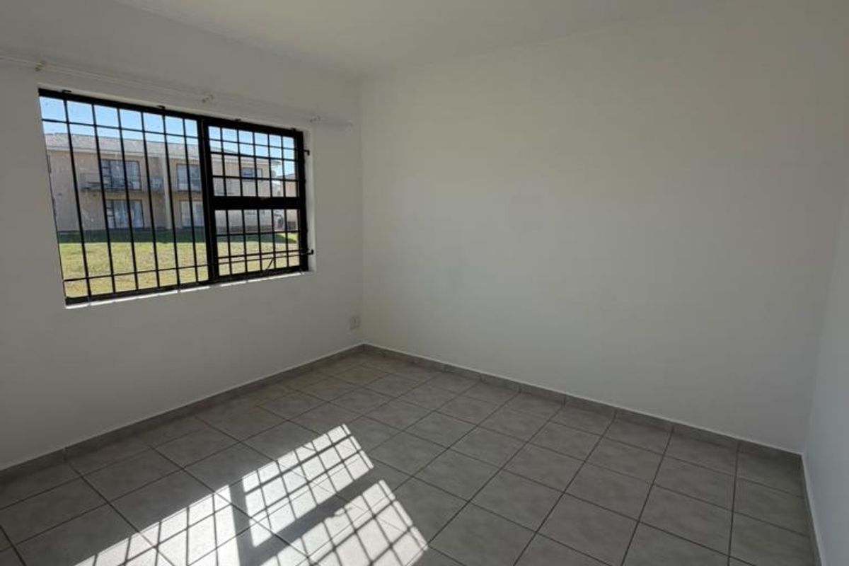 A bright, empty bedroom featuring neutral tiled flooring and a window fitted with security bars, offering a clean canvas for interior design.
