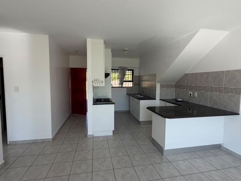 An open-plan kitchen featuring granite countertops, a built-in hob with extractor fan, tiled backsplash, and neutral ceramic floor tiles.
