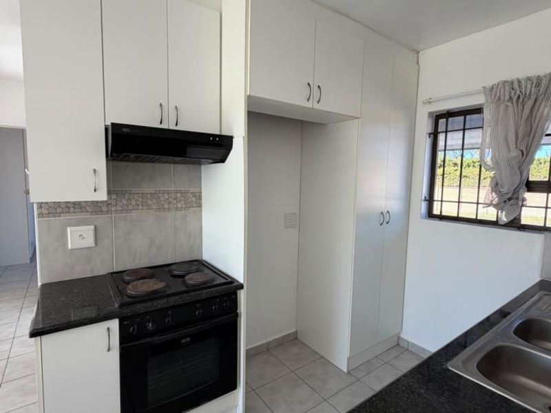 A clean, functional kitchen featuring white built-in cabinetry, granite countertops, an integrated stove and oven, and tiled flooring with natural light.