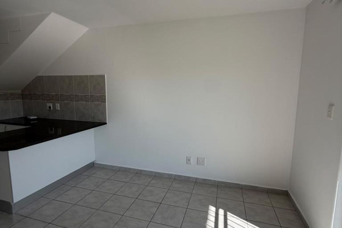 A clean, empty kitchen area featuring neutral ceramic floor tiles, a granite countertop, and a tiled backsplash, ready for customization.