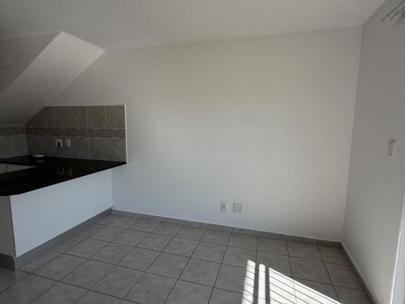 A clean, empty kitchen area featuring neutral ceramic floor tiles, a granite countertop, and a tiled backsplash, ready for customization.