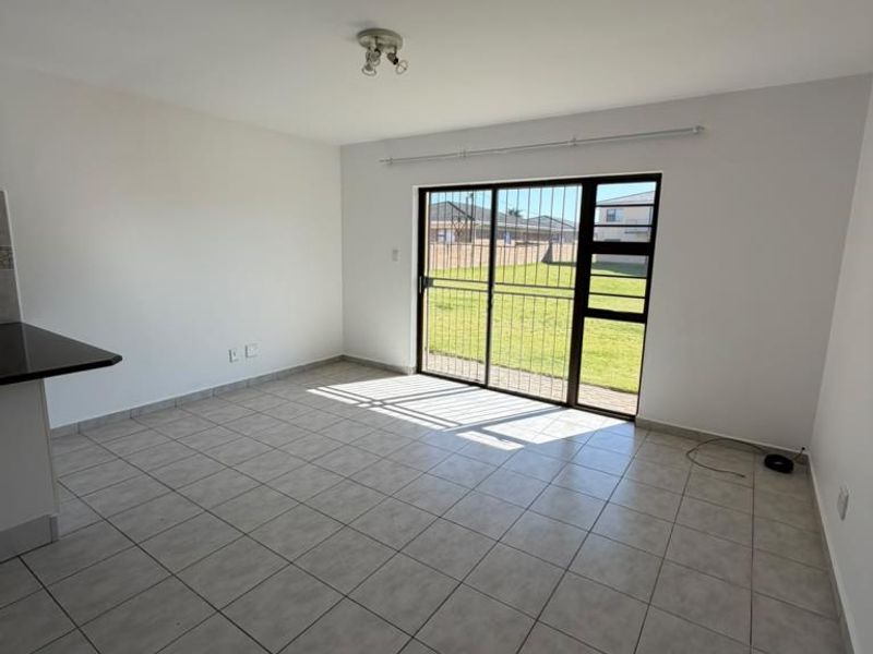 Bright open-plan living area featuring neutral tiled flooring and a large sliding glass door with security gate providing access to the rear garden.