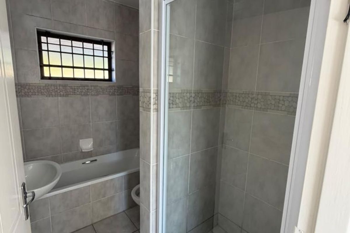 A clean, functional bathroom featuring a separate shower enclosure, bathtub, basin, and neutral wall and floor tiling.