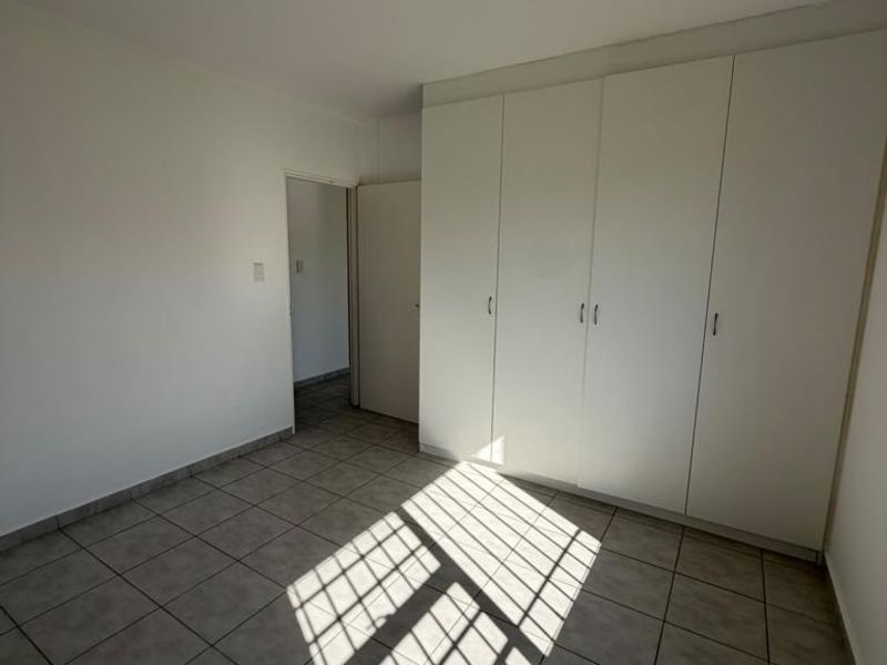 An empty bedroom featuring neutral tiled flooring and ample built-in cupboard storage space.