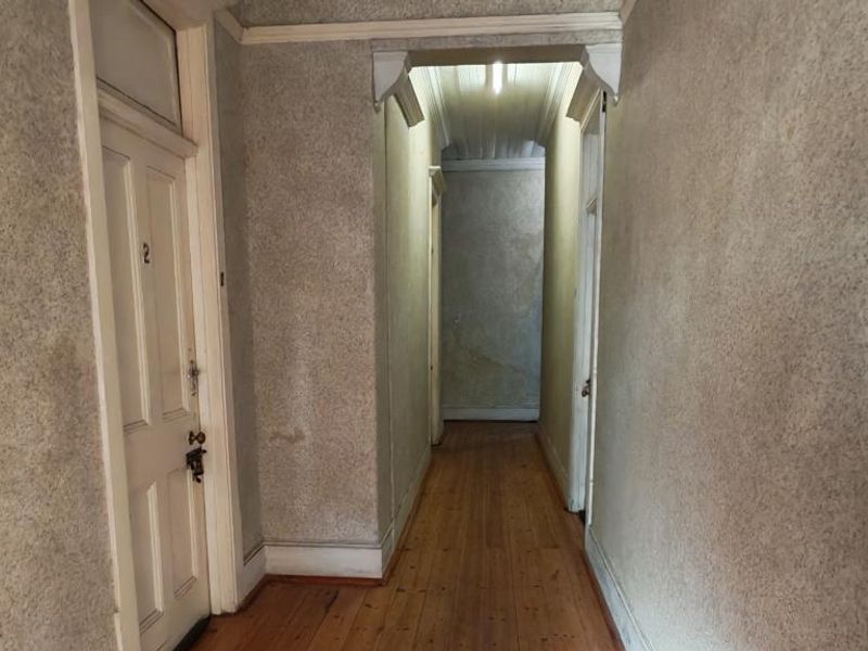 A narrow interior hallway featuring original timber flooring and panelled doors, requiring cosmetic updates to the wall finishes.