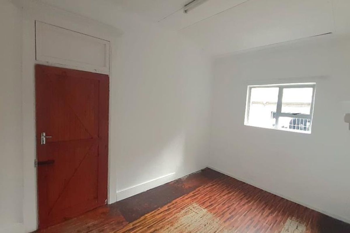 An empty bedroom featuring timber flooring, a wooden door, and a window, offering a blank canvas for renovation or staging.