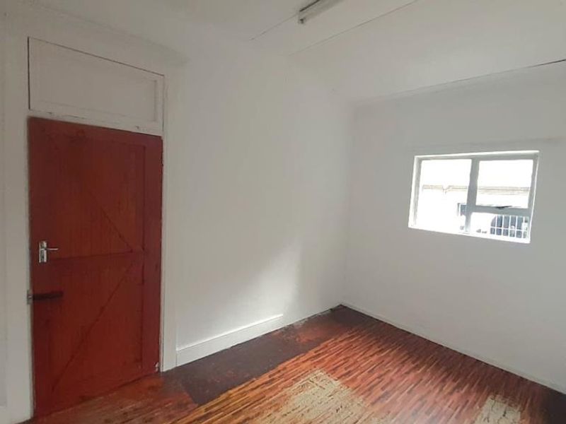 An empty bedroom featuring timber flooring, a wooden door, and a window, offering a blank canvas for renovation or staging.