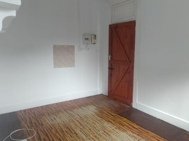An empty living room featuring original parquet flooring, a timber door, and visible electrical infrastructure, ready for renovation or staging.