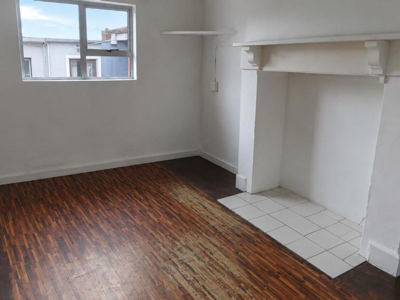 An empty living room featuring a traditional fireplace mantel, tiled hearth, and original parquet flooring in need of restoration.