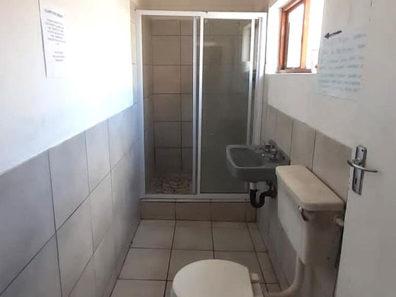 A compact, functional bathroom featuring a shower enclosure, wall-mounted basin, and toilet with tiled walls and flooring throughout.