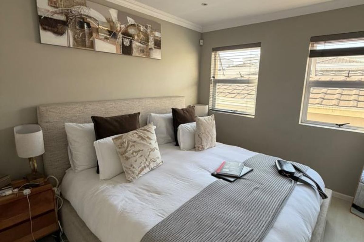 A well-maintained bedroom featuring neutral wall tones, laminate flooring, recessed lighting, and large windows with fitted blinds.