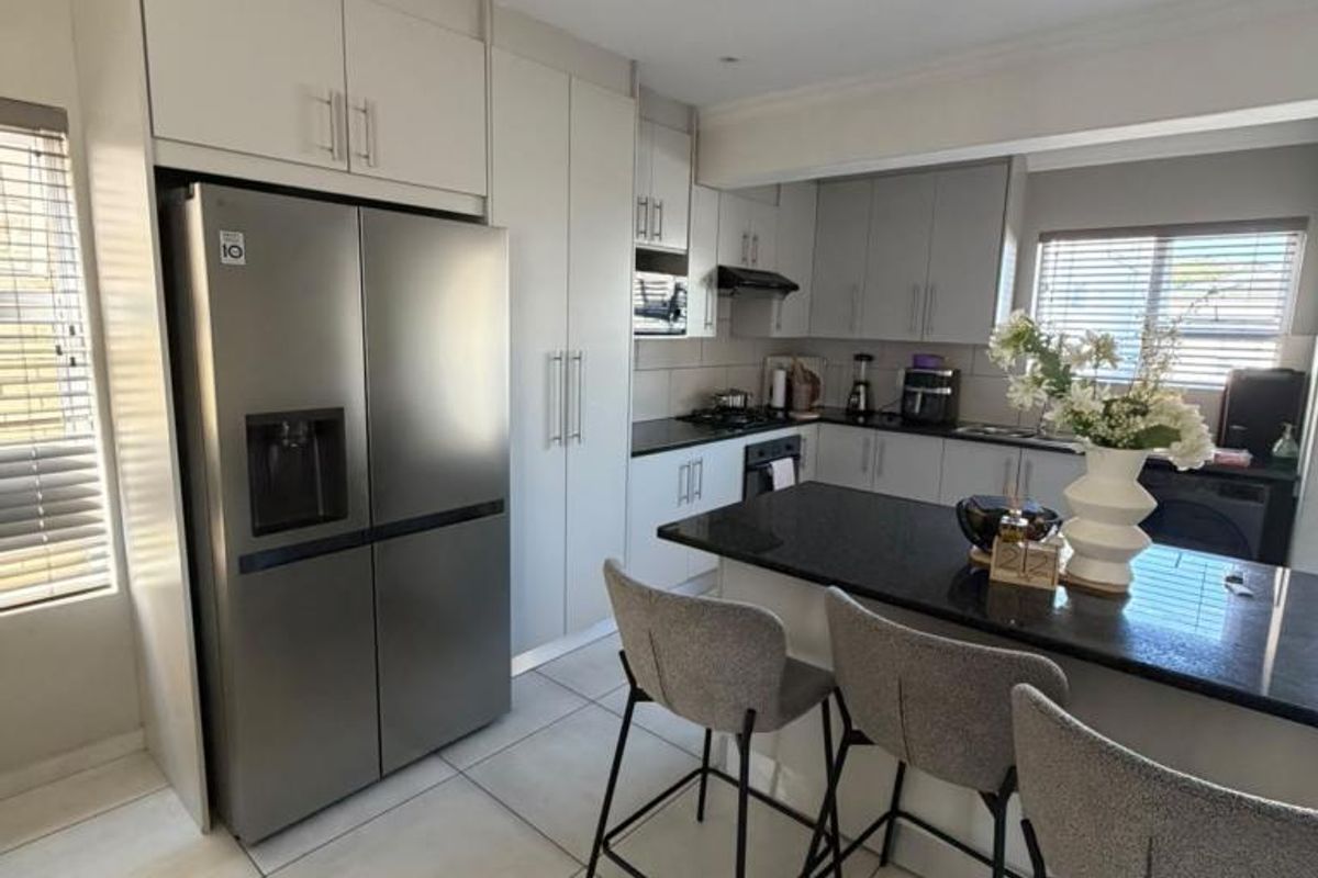 Modern kitchen featuring sleek cabinetry, granite countertops, a central island, and integrated appliances, finished with neutral tiled flooring.